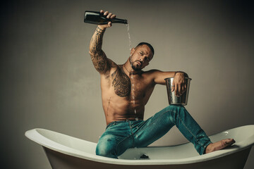 Sexy undress man sit on bathtub in bathroom, men holiday with champagne. Celebrating christmas or birthday. Private sex party. - obrazy, fototapety, plakaty