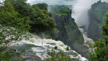 The Zambezi River flows into the gorge, bubbling and foaming. The rapid flow of water between the...