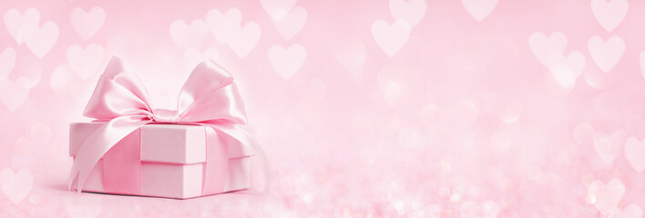 Pink gift box with shining pink ribbon bow on pink hearts bokeh background. Gift or holiday...