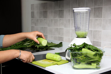 Preparation of green juice, the vegetables are chopped on the wooden board and put in the blender in the kitchen for healthy and dietary breakfast
