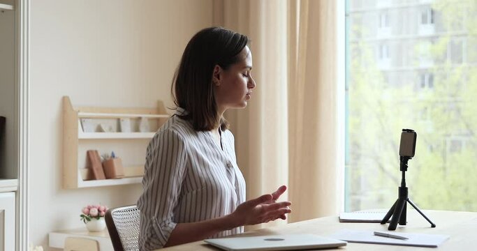 Video lesson. Young female school teacher broadcast remote class live speak to pupils explain new material before cell webcam. Millennial lady having distant job interview using phone fixed on tripod