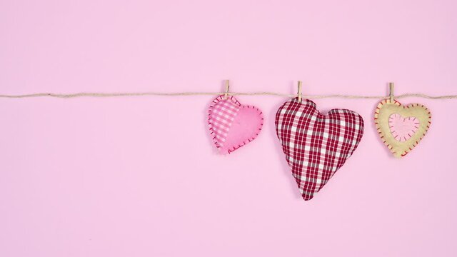 Three softy hearts hanging on rope on pastel pink theme. Stop motion