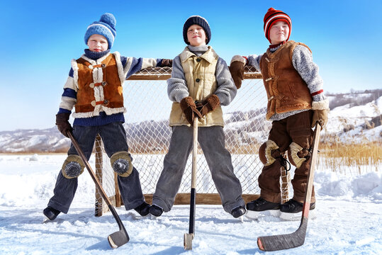 Children play hockey. Team of young boys are engaged in active winter sports on the ice of the lake against the background of a snow landscape on a sunny day. Art photography in retro style.