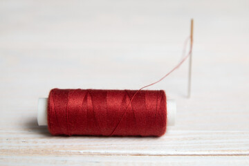 A spool of red thread and a needle on a light background.