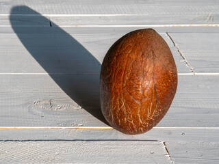 Whole ripe coconut without a hard peel with shadow on white wooden background, close-up