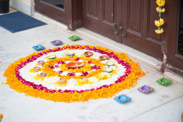 Rangoli pookalam pattern made of flower petals with handmade diya lamps around it on the ground for religious celebrations like diwali, christmas and new year