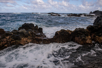 Fototapeta na wymiar Cooled black lava beaten by the Atlantic ocean waves. View of sea waves hitting rocks on the beach. Waves and rocks.
