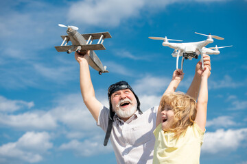 Excited grandson child and funny amazed grandfather with plane and quadcopter drone over blue sky...