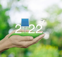 2022 white text with solar cell on green grass field in man hands over blur forest, Happy new year 2022 ecological cover concept