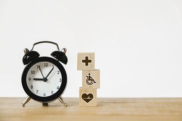health and medical icon on wooden block and  black analog alarm clock on wood desk for health insurance, nonstop medical service, emergency case,  wellness, wellbeing concept