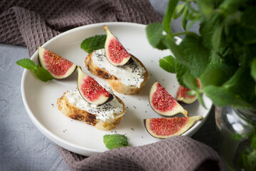 Healthy sandwiches with fresh figs and cream cheese, mint leaves, white  plate, gray background, empty space