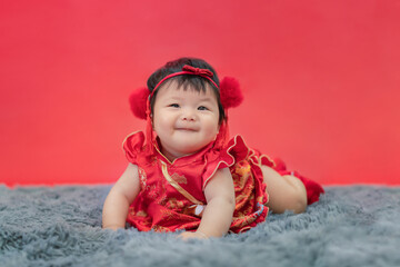Asian Chinese baby girl crawling, smiling and laughing on carpet as red background. Happy cute Asian infant baby crawling in a living room as concept of Chinese New Year.