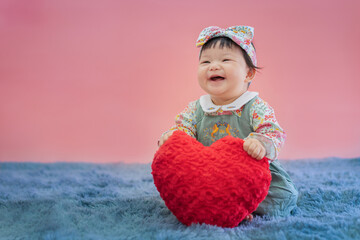 Asian baby valentine with red heart smiling and sitting on pink background. Cute 6 months baby...