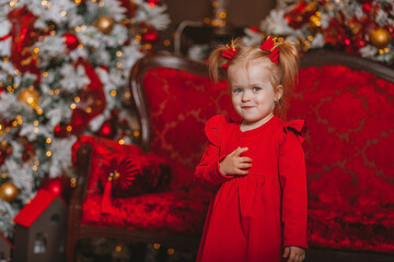 charismatic little girl in a red dress on the background of Christmas decorations	 
