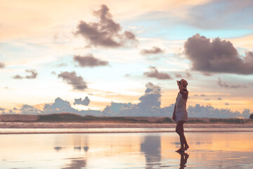 Rear view of young adult tourist asian woman walking relax on beach sand with beautiful dramatic sunset sky