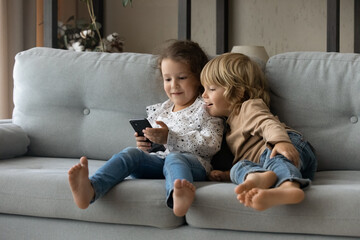 Sweet little sibling gen Z kids using online app on smartphone, browsing internet, playing funny...