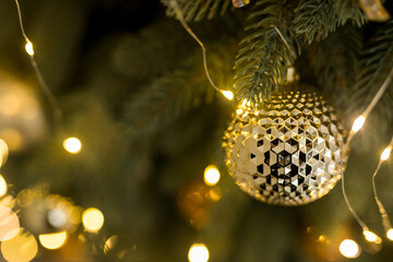 Close up of holidays location with gold ball toy and garlands on green Christmas tree