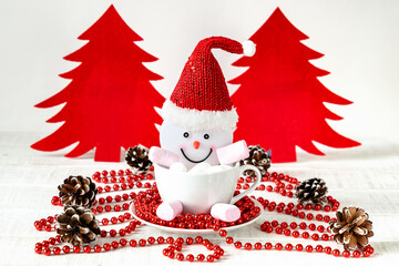 Snowman and marshmallows in cup, red felt christmas tree on white table