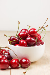 Cherries in a white bowl on a wooden background.