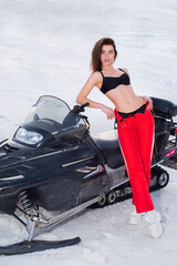 Fototapeta na wymiar Sexy woman posing with snowmobile in snowy winter. Snow mobile girl driving. Winter fun.