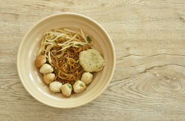 dry Chinese yellow egg noodles dressing black sweet soy sauce with pork meatball and bean sprout in soup on bowl