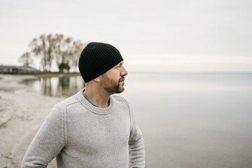 Bearded man in beanie staring out over a calm winter ocean