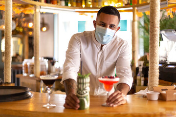 Elegant young Latin American bartender serving a cocktail at the bar of a modern cocktail bar. He...