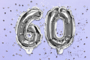 Silver foil balloon number, digit sixty on a lilac background with sequins. Birthday greeting card with inscription 60. Anniversary concept. Top view. Numerical digit. Celebration event, template.