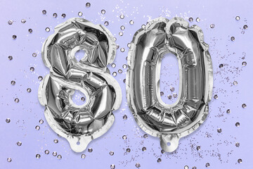 Silver foil balloon number, digit eighty on a lilac background with sequins. Birthday greeting card with inscription 80. Anniversary concept. Top view. Numerical digit. Celebration event, template.