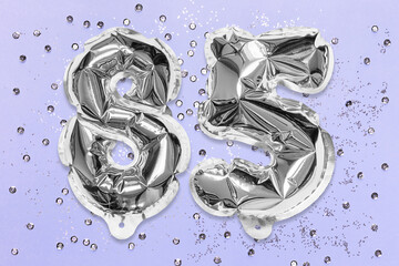 Silver foil balloon number, digit eighty five on a lilac background with sequins. Birthday greeting card with inscription 85. Anniversary concept. Numerical digit. Celebration event, template.