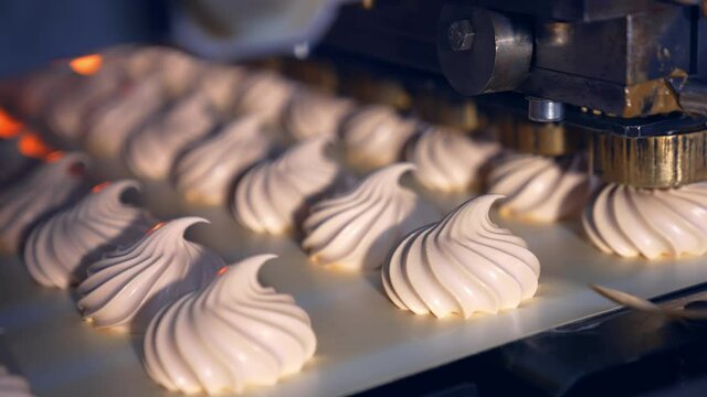 Creamy marshmallows being squeezed onto the conveyor belt. Well-coordinated work of the molding machine producing tasty sweets. Process in close up.