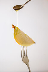 Onion with honey on a fork, close-up. On white background. Creative