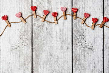 Red hearts on rope with clothespins, on a wood background