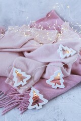 Pink cashmere products are decorated with Christmas lanterns, on a light background, the concept of winter comfort, home warmth and celebration