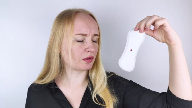 Hypomenorrhea. The woman shows a gynecological pad with a small drop of blood on it. Concept of small amounts during scanty menstruation. Complaints of pain and strange cycle. Diseases in gynecology