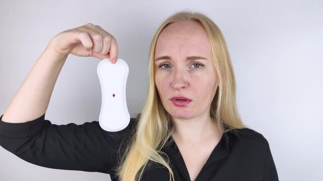 Hypomenorrhea. The woman shows a gynecological pad with a small drop of blood on it. Concept of small amounts during scanty menstruation. Complaints of pain and strange cycle. Diseases in gynecology