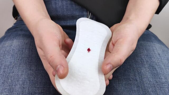 Hypomenorrhea. The woman shows a gynecological pad with a small drop of blood on it. Concept of small amounts during scanty menstruation. Complaints of pain and strange cycle. Diseases in gynecology