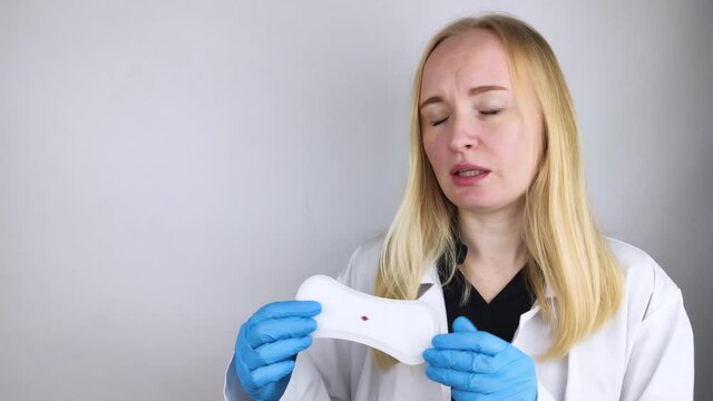 Hypomenorrhea. The woman shows a gynecological pad with a small drop of blood on it. Concept of small amounts during scanty menstruation. Complaints of pain and strange cycle. Diseases in gynecology