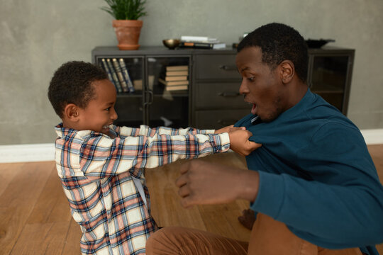 Profile picture of uncle and nephew playing together in living-room, boy pulling his jumper, pretending fighting, having fun, enjoying moment. Human relationships. Father and son bonding