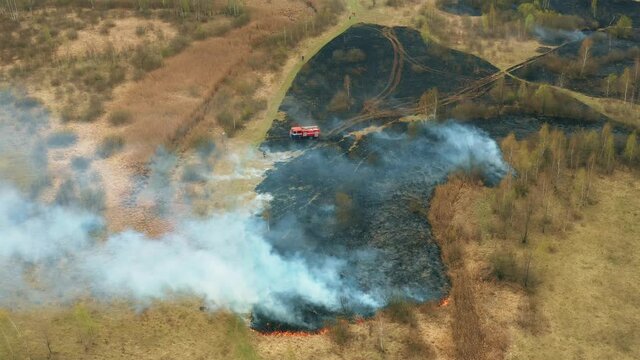 4K Aerial View Spring Dry Grass Burns During Drought Hot Weather. Bush Fire And Smoke. Fire Engine, Fire Truck On Firefighting Operation. Wild Open Fire Destroys Grass. Ecological Problem Air