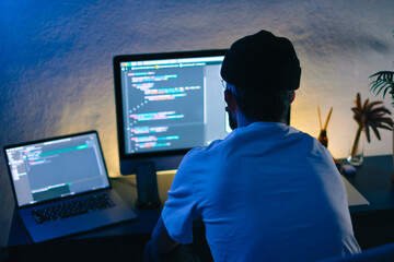 Young man mobile developer writes program code on a computer, programmer work in home office.