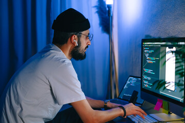 Young man mobile developer writes program code on a computer, programmer work in home office.