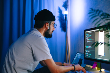 Young man mobile developer writes program code on a computer, programmer work in home office.