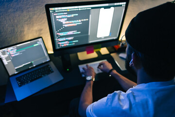 Young man mobile developer writes program code on a computer, programmer work in home office.