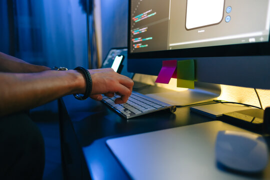 Mobile developer writes program code on a computer, typing on keyboard, programmer work in home office.