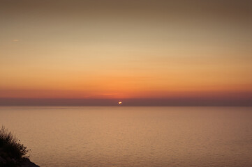 Sun at horizon disappearing behind the clouds as it sets over the sea in Zakynthos island, Greece