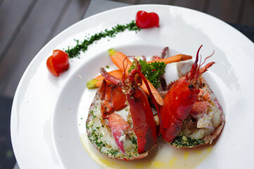 baked american lobster with basil pesto and cherry tomatoes on round white plate top view