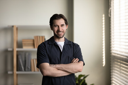 Happy confident millennial business man in casual, company leader, founder, professional posing with arms folded, looking at camera, smiling. Businessman indoor head shot portrait
