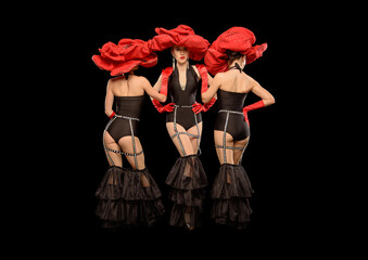 Three beautiful cabaret dancers in red hats isolated on black