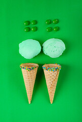 Ice cream, waffle cones and candy drops on green background. Flat lay composition